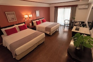 A hotel room with two beds, a desk, a chair, and a potted plant.