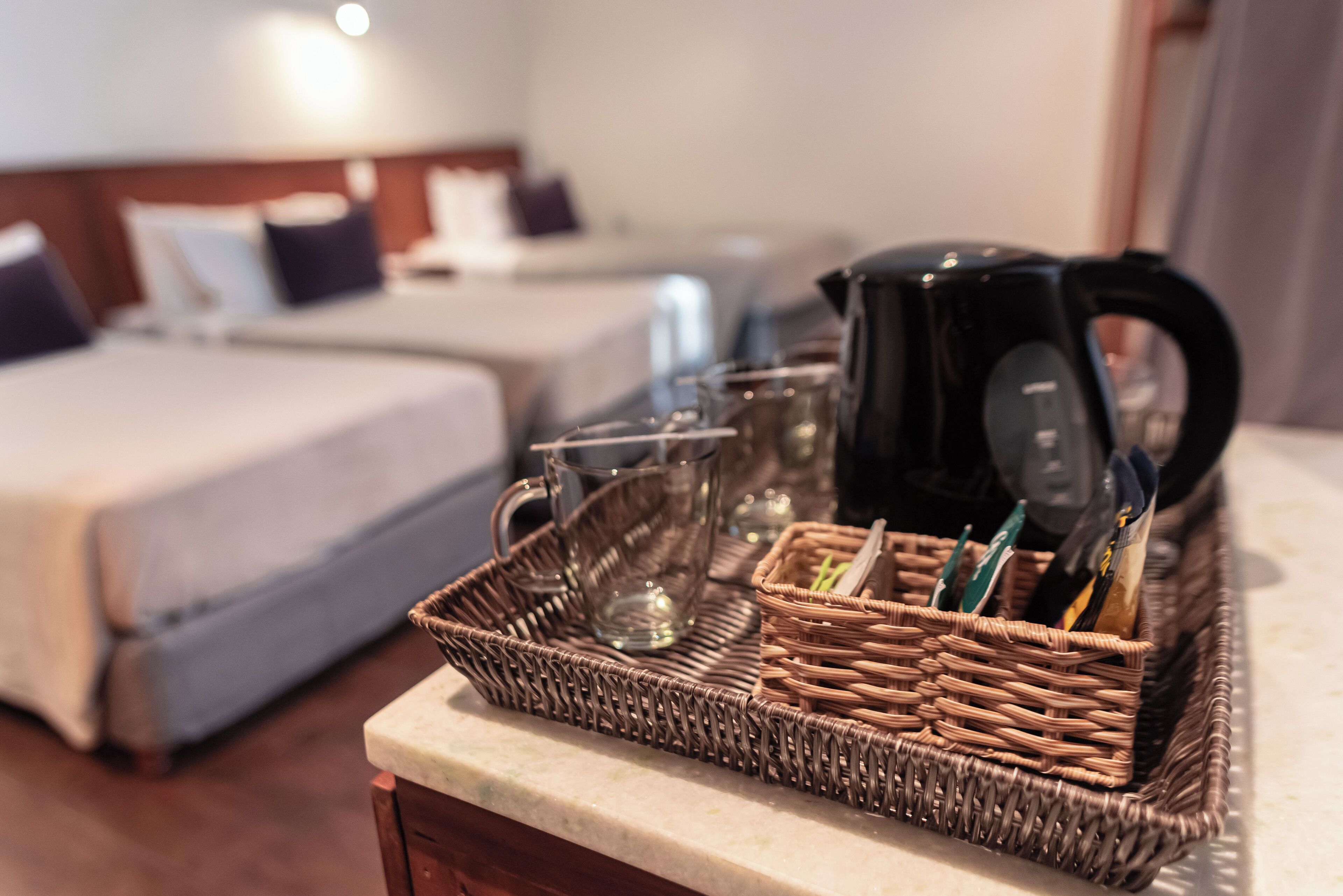 Ein Korbtablett mit Kaffeemaschine, Gläsern und Spielkarten auf einer Hotelzimmer-Anrichte.