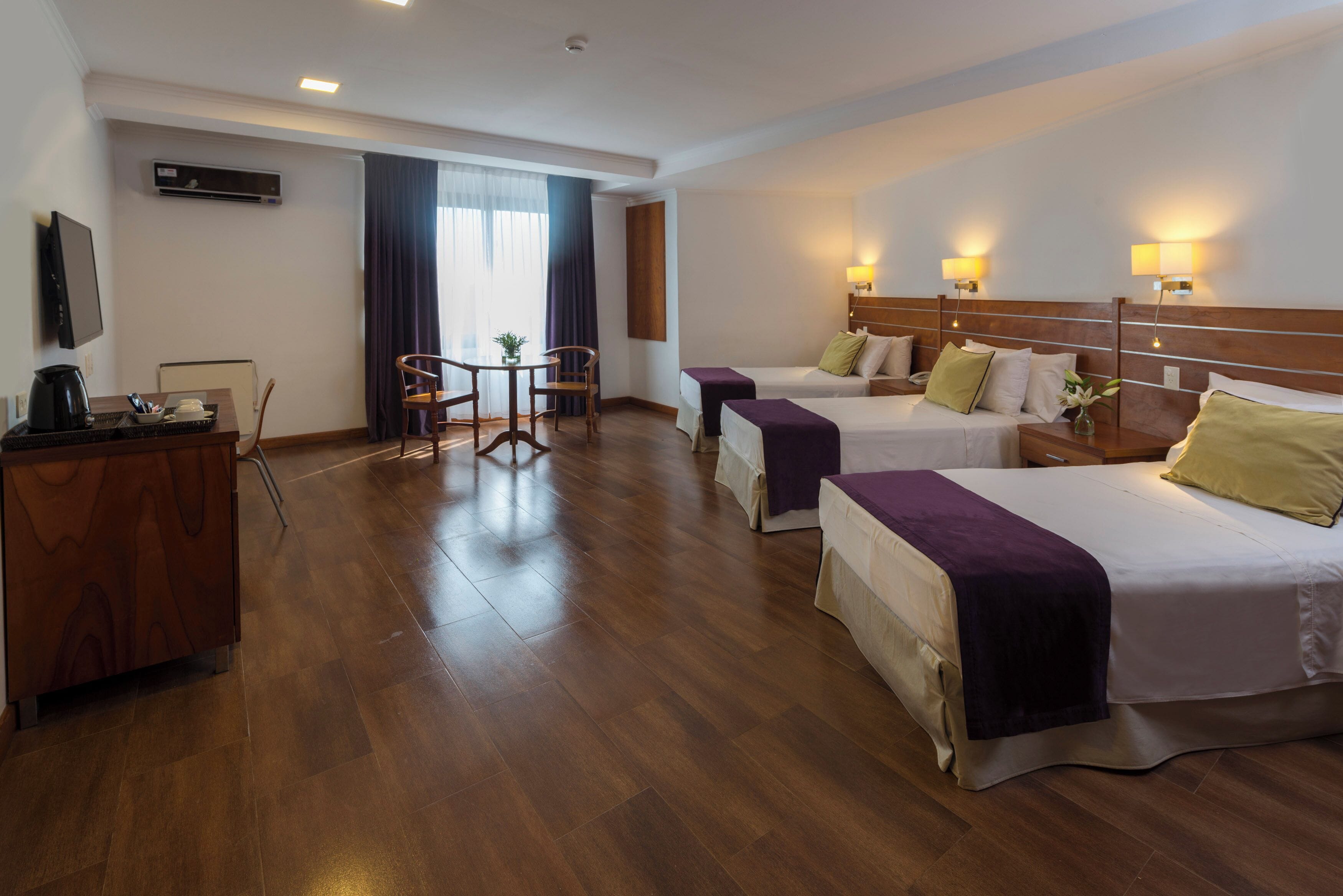 Habitación de hotel con dos camas, un escritorio, una silla y un televisor.