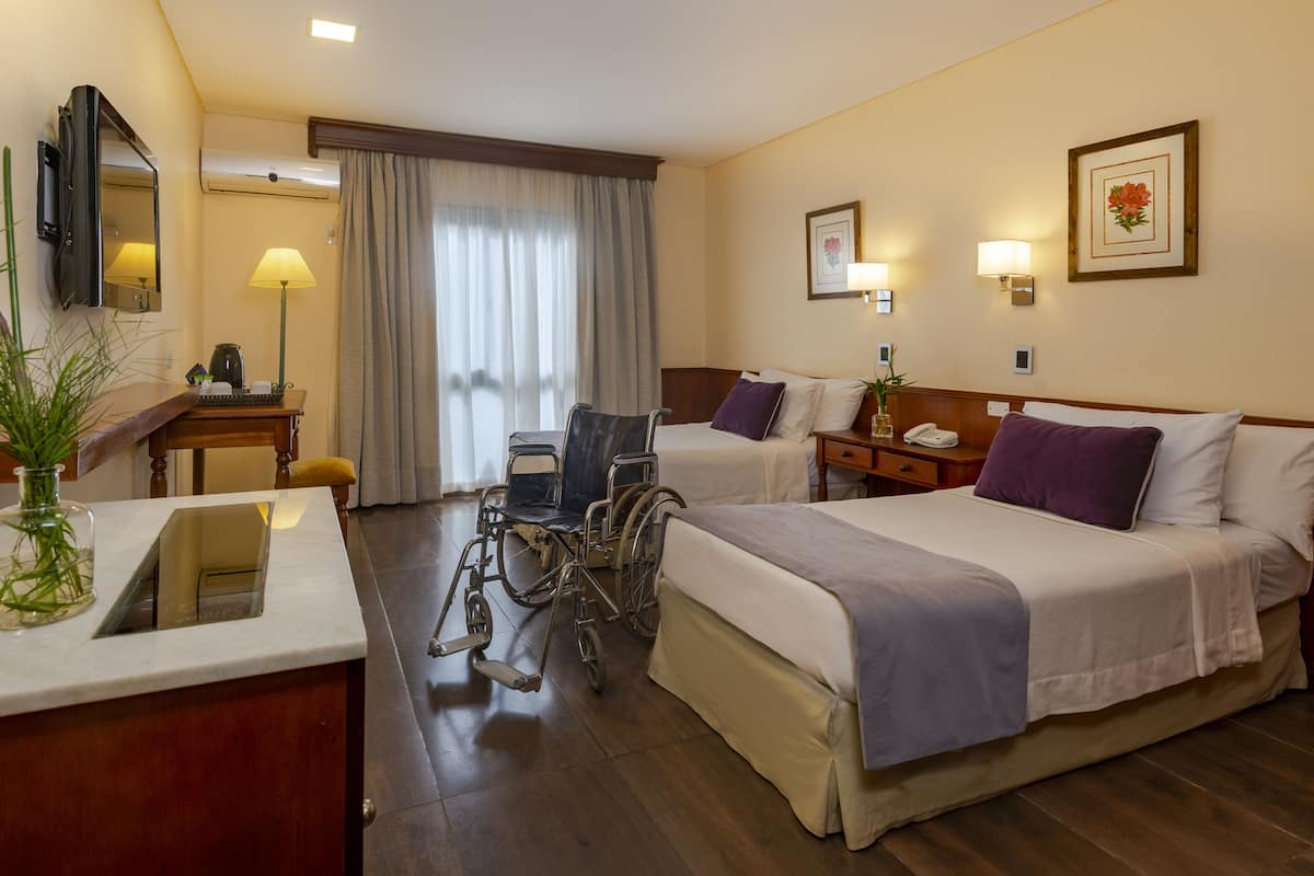 Ein Hotelzimmer mit Bett, Schreibtisch, Rollstuhl, Sessel und Bad.