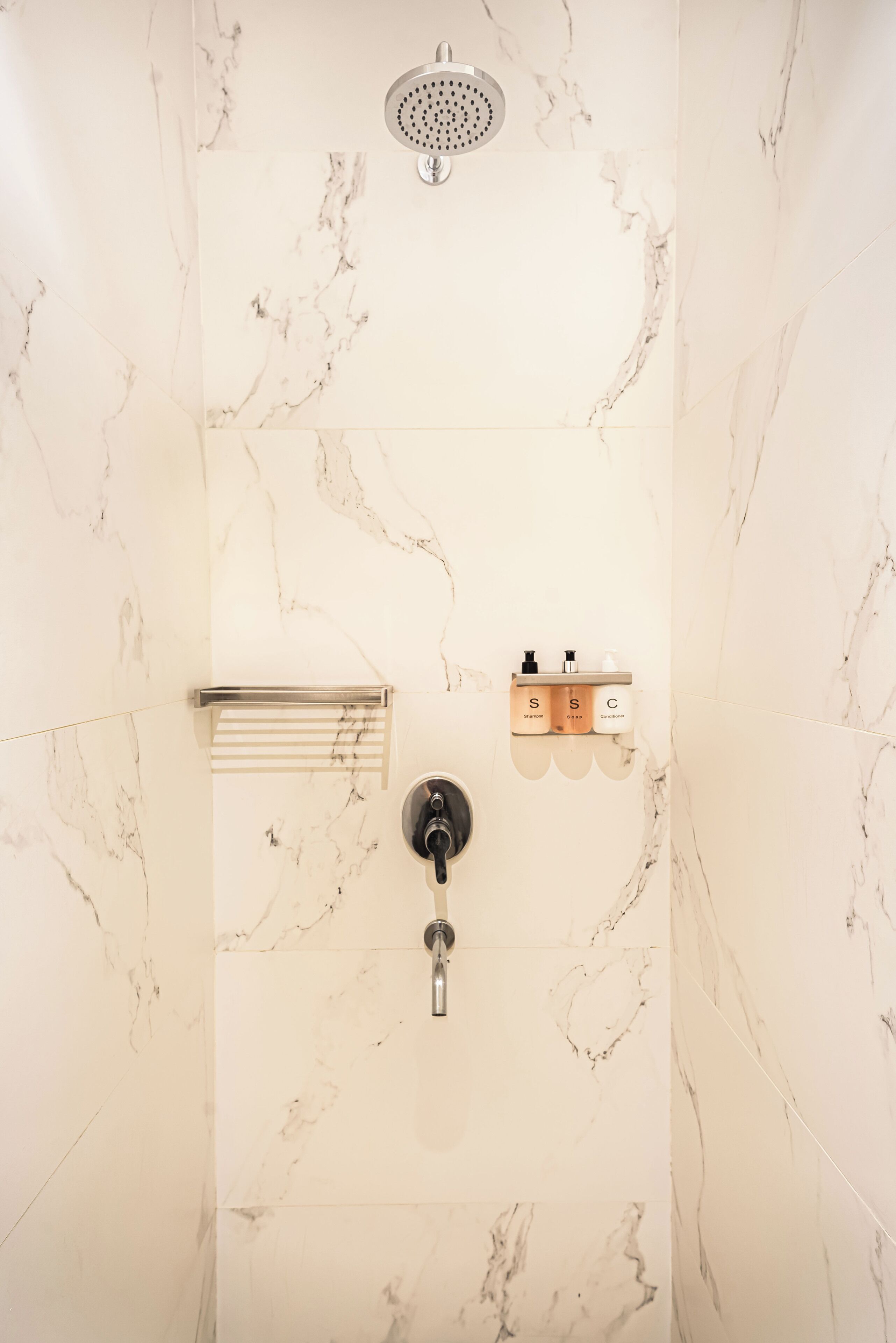 Un baño con ducha, paredes de mármol, un perchero y un estante con artículos de aseo.