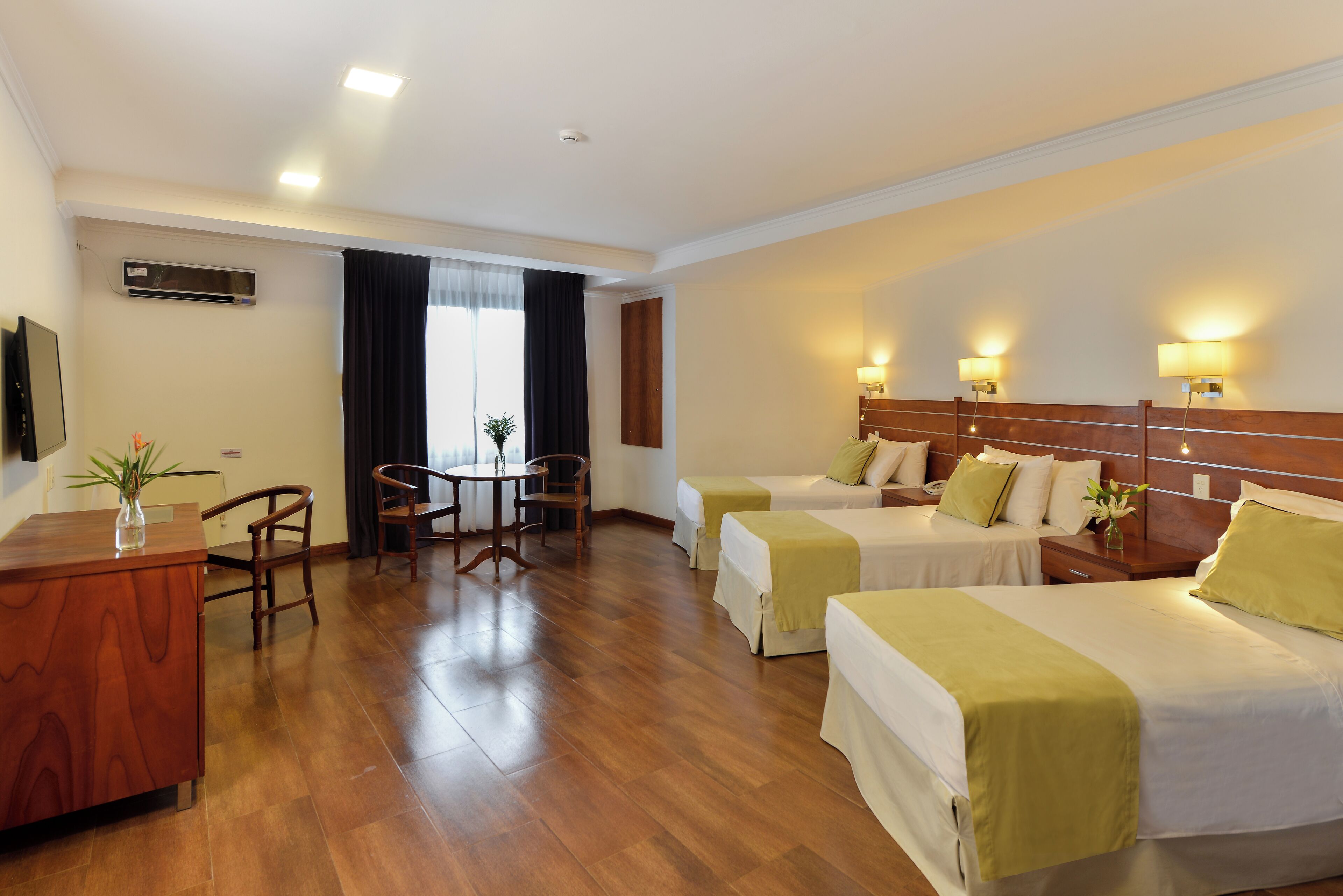 A hotel room with two beds, a desk, a chair, a table, and a TV.
