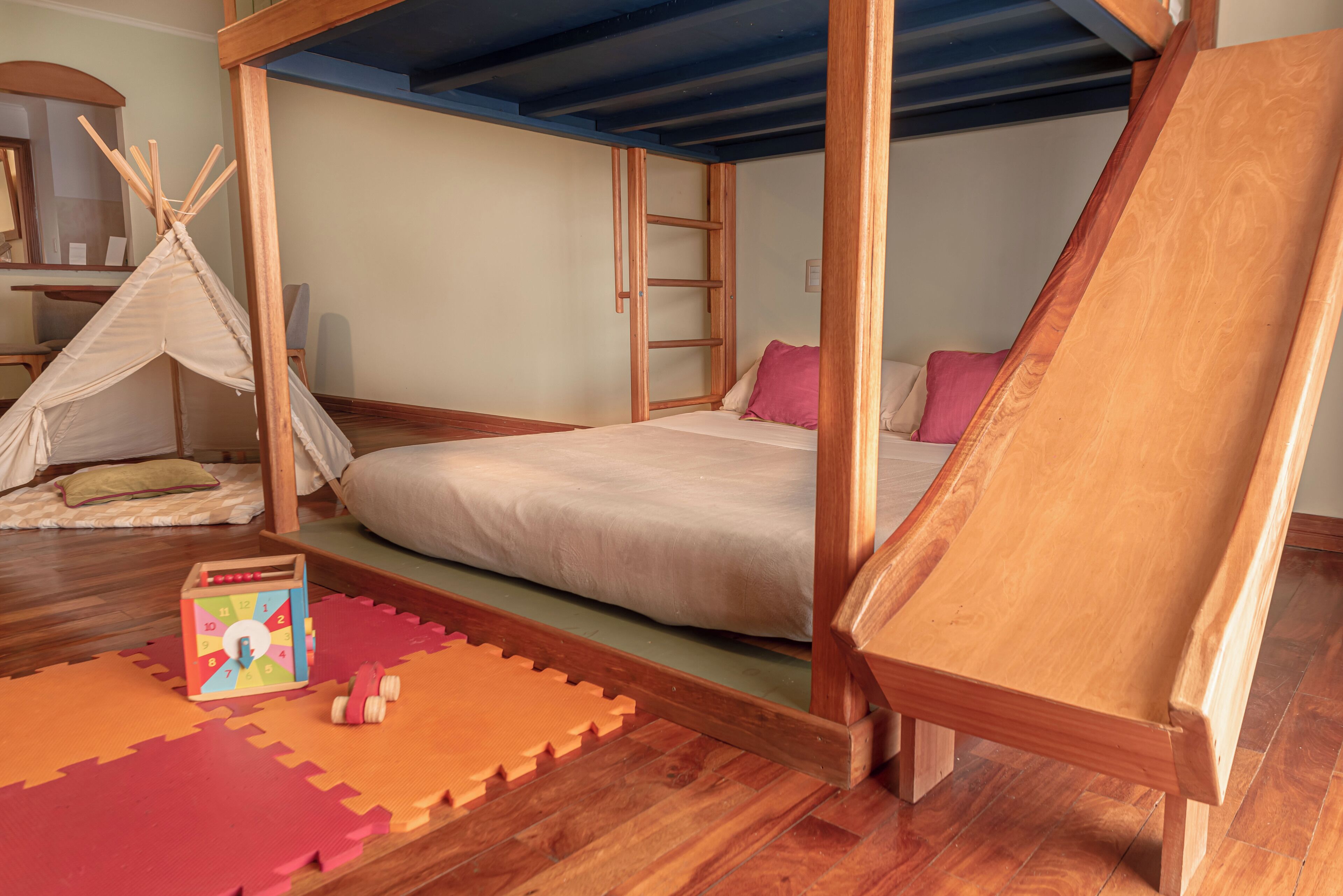 A bedroom with a wooden bunk bed, a small wooden ladder, a teepee, and a colorful toy.