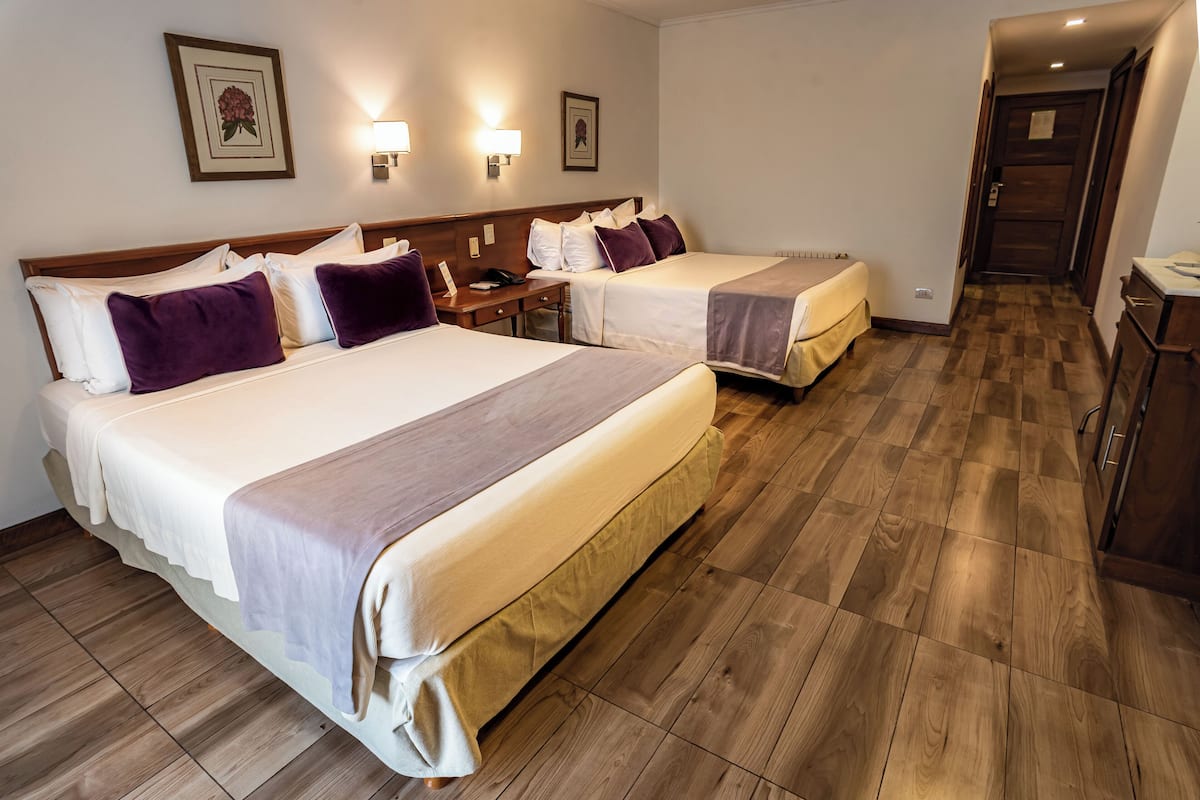 Ein Hotelzimmer mit zwei Betten, Holzboden und einem Schreibtisch mit Stuhl.