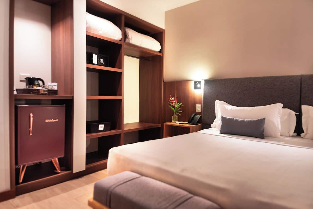 Ein Hotelzimmer mit einem großen Bett, einem Kleiderschrank, einem Nachttisch mit Lampe und einem kleinen Schreibtisch mit Telefon.