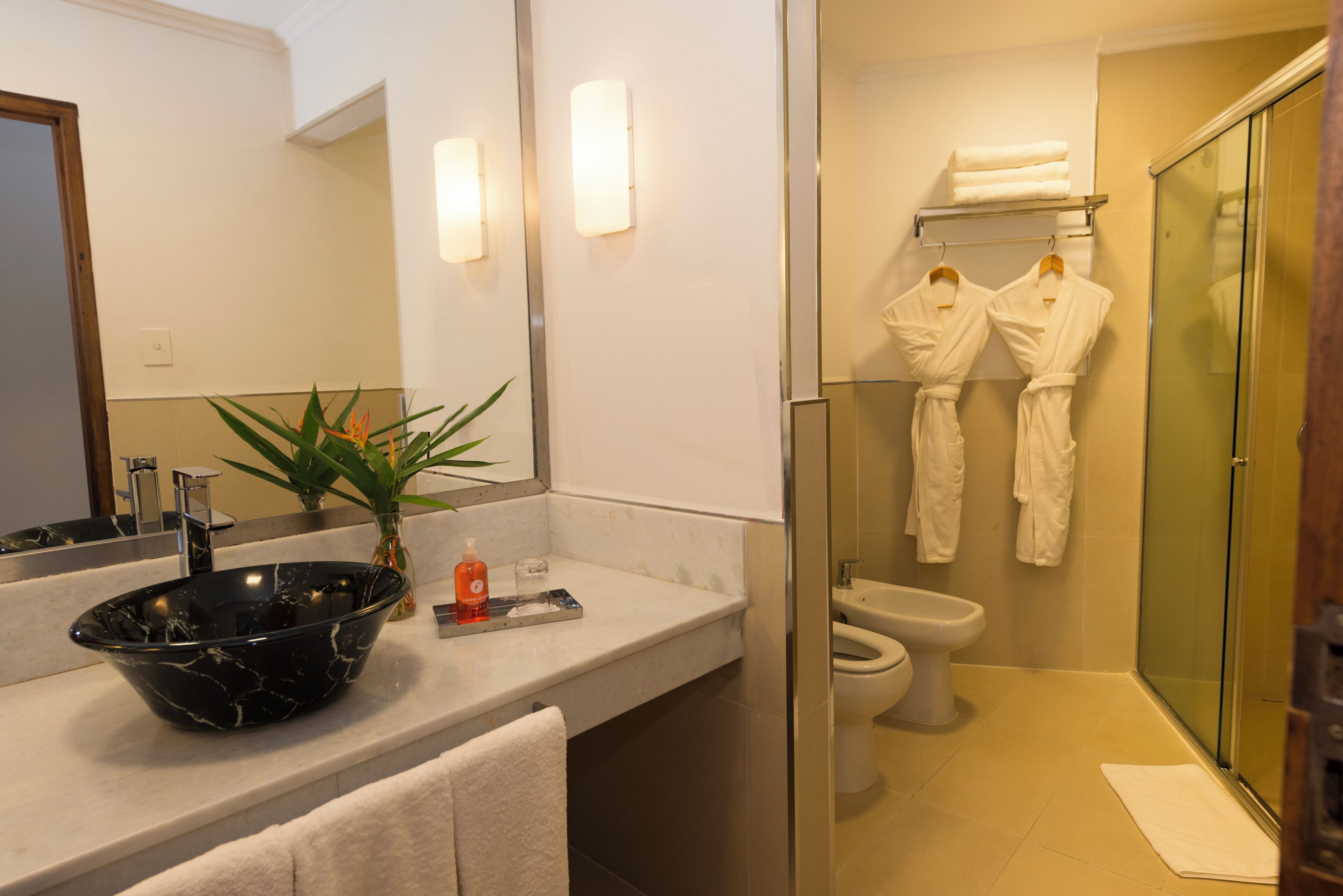 A modern bathroom with a black marble sink, a glass shower enclosure, and white towels.