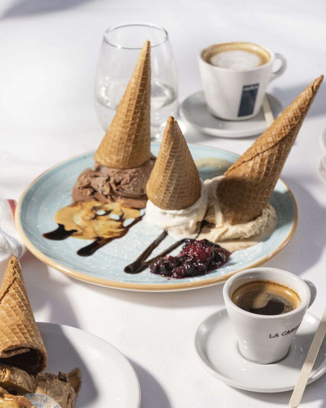 A dessert plate with ice cream cones, a glass of a beverage, and a cup of coffee on a table.