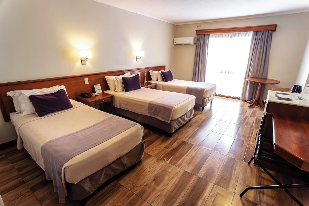 Ein Hotelzimmer mit zwei Betten, einem Schreibtisch und einem Stuhl. Zwei Nachttische mit Lampen sowie ein kleiner Tisch mit einem Stuhl sind ebenfalls vorhanden.