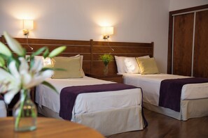 A hotel room with two beds, wooden headboard, bedside lamps, a vase with flowers, and a wardrobe.