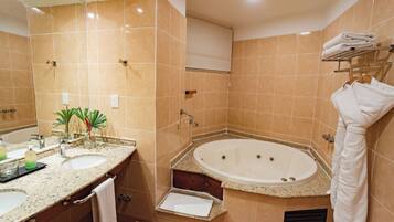 Ein Badezimmer mit einer großen Badewanne, einem Waschbecken und einem Spiegel. Ein Handtuchhalter mit Handtüchern und eine Pflanze befinden sich auf der Ablagefläche.