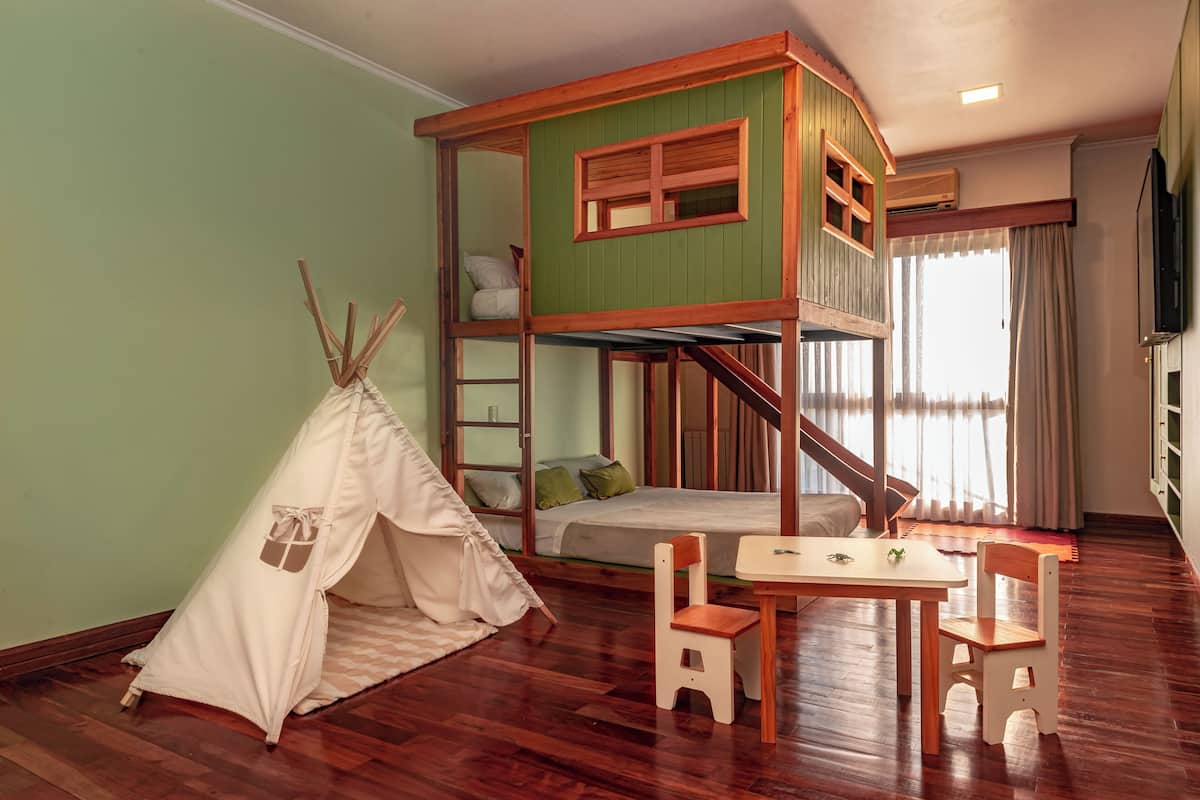 Ein Zimmer mit einem Etagenbett, einem kleinen Tisch mit Stühlen, einer zeltartigen Konstruktion und einer Treppe.