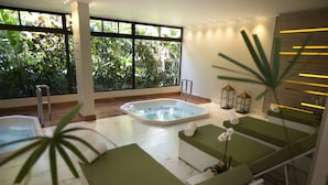 Uma sala de spa moderna com hidromassagem, assentos acolchoados verdes e janelas amplas com vista para um jardim.