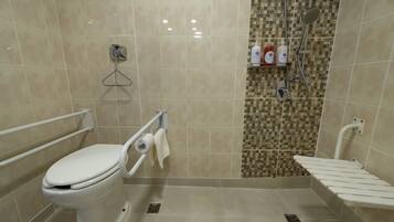 Un baño con inodoro, barras de apoyo, zona de ducha con pared de azulejos y estante con artículos de aseo.