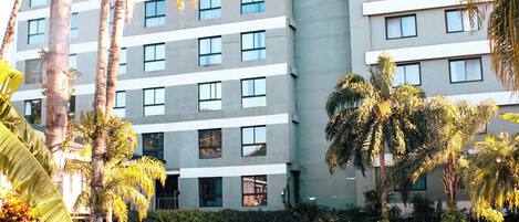 A hotel with a swimming pool, lounge chairs, and palm trees.