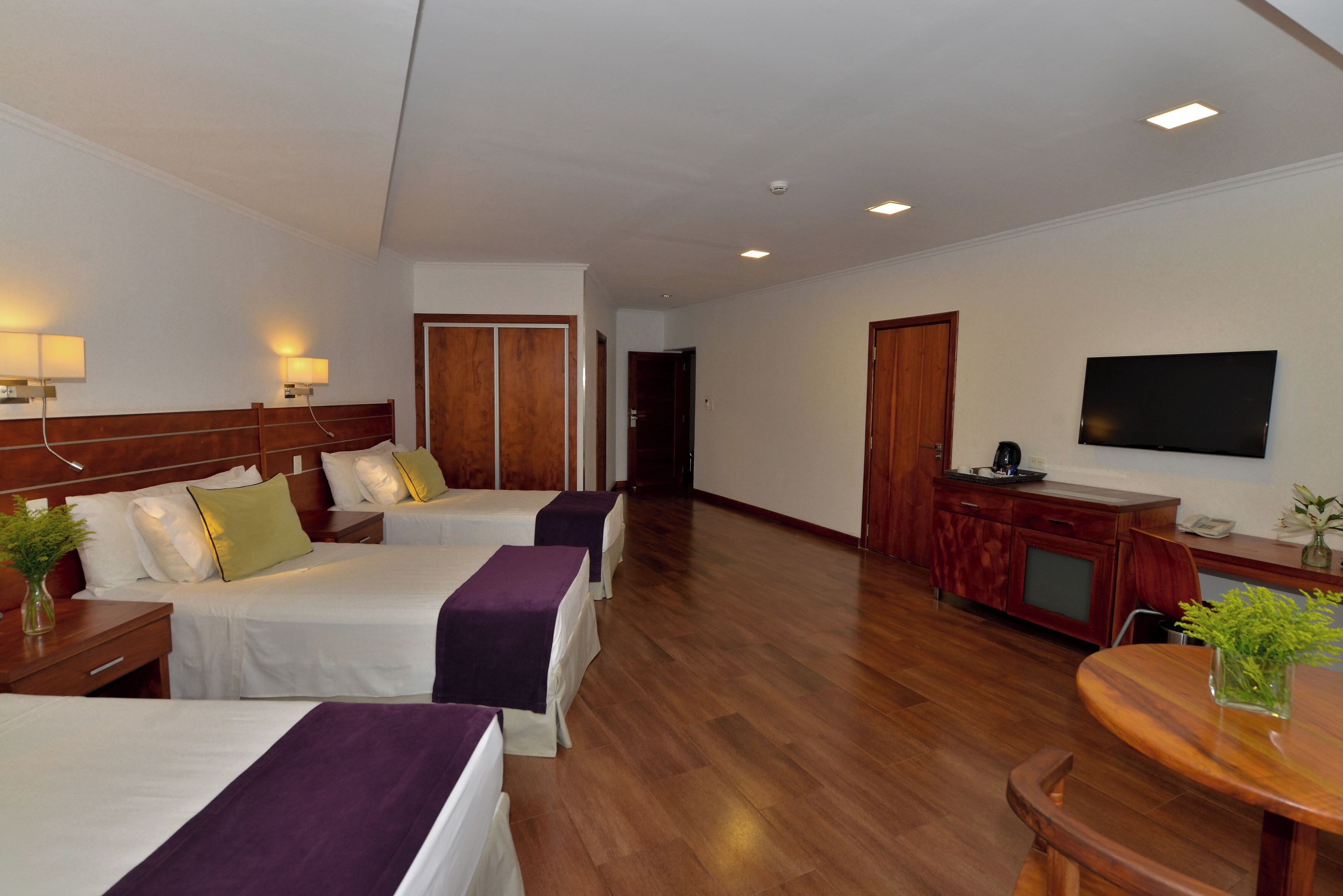 Habitación de hotel con dos camas, un escritorio de madera, un televisor y una mesa de comedor.