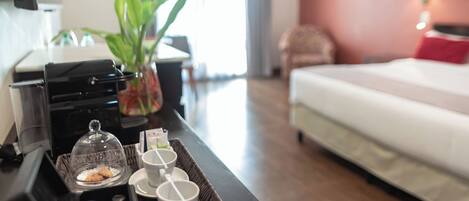 Una habitación de hotel con cama, una mesa de comedor con una bandeja de café y pasteles, una planta y un televisor.