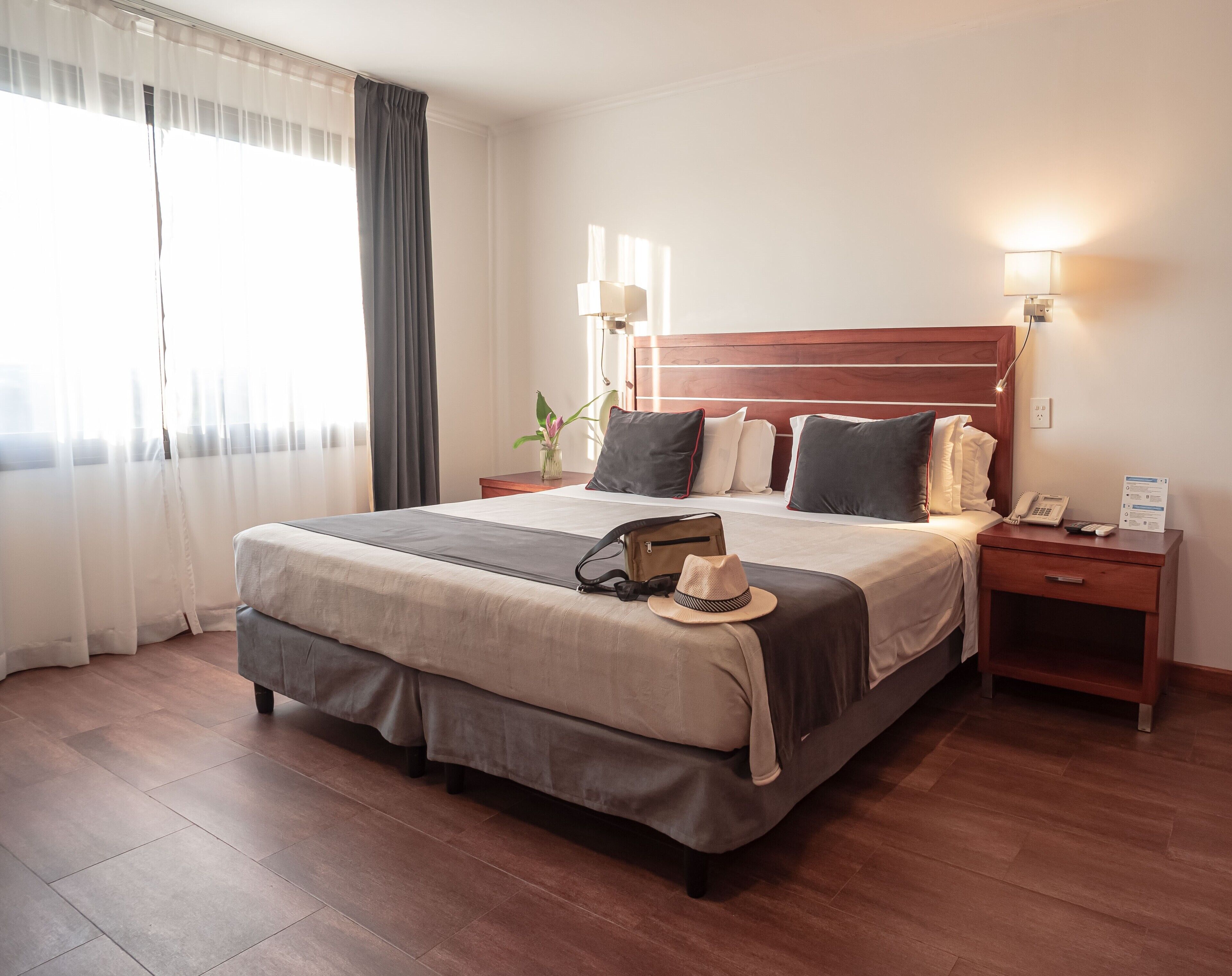 A hotel room with a large bed, bedside lamps, a nightstand with a phone, and a window with curtains.