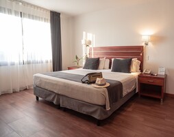 Habitación de hotel con una cama grande, lámparas de noche, una mesita de noche con un teléfono y una ventana con cortinas.