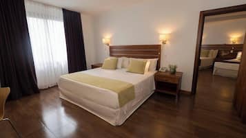 Ein Hotelzimmer mit einem großen Bett, zwei Nachttischen, einem Spiegel und einem Fenster mit Vorhängen.