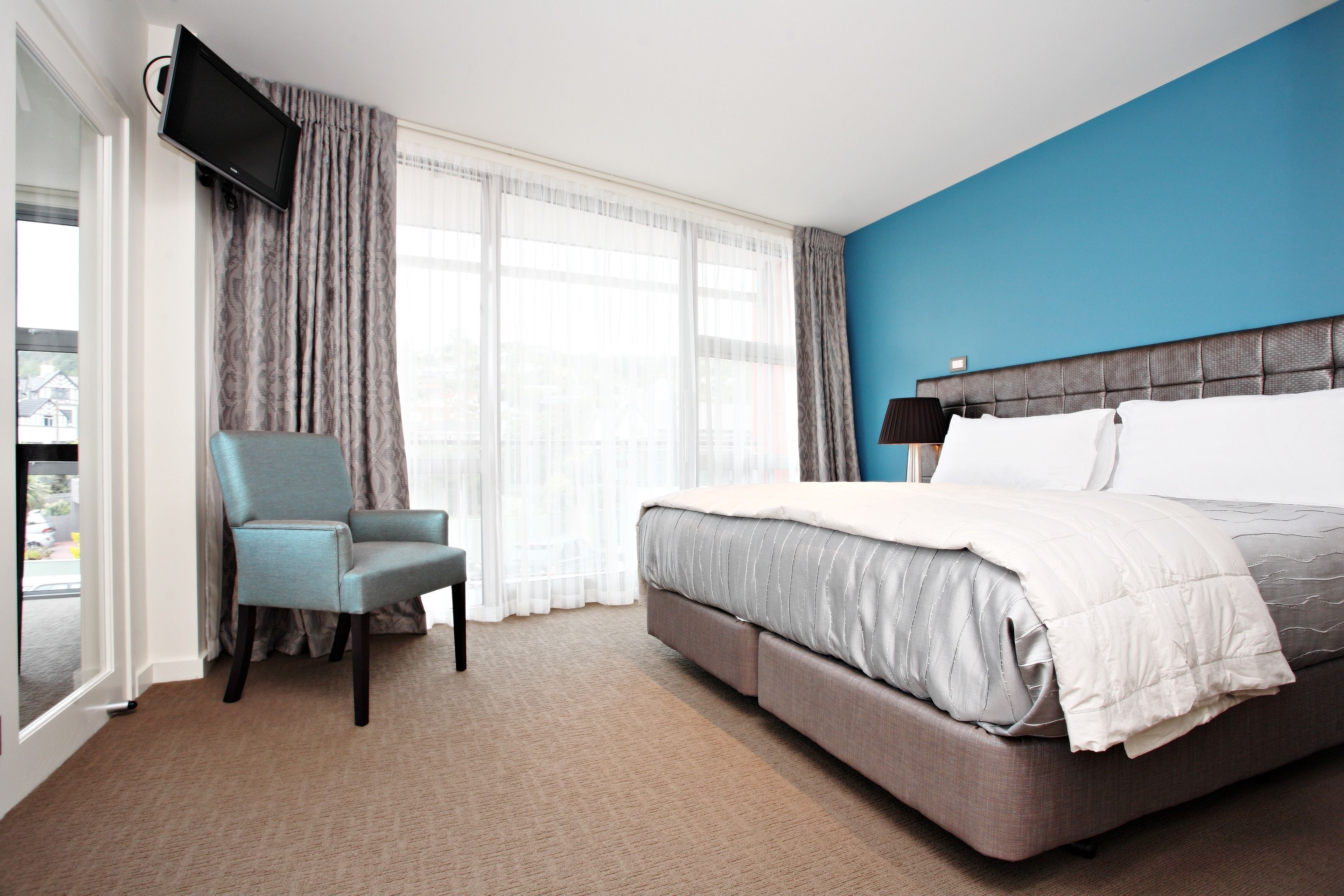 A hotel room with a large bed, a chair, a television, and a view of the outside.