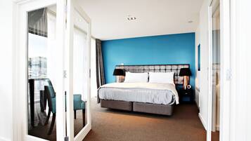 A hotel room with a bed, a nightstand, a lamp, and a view of the city through a glass door.