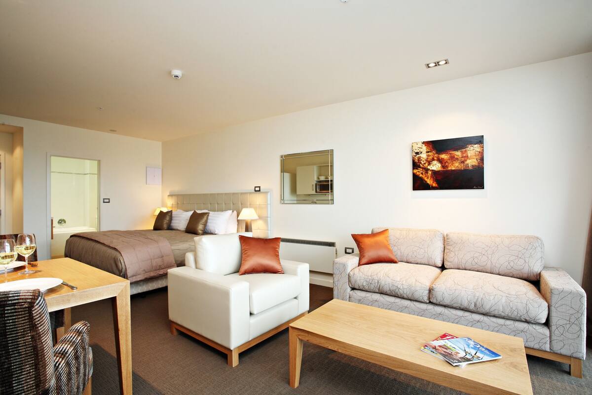 A modern hotel room with a bed, two sofas, a dining table, and a coffee table.
