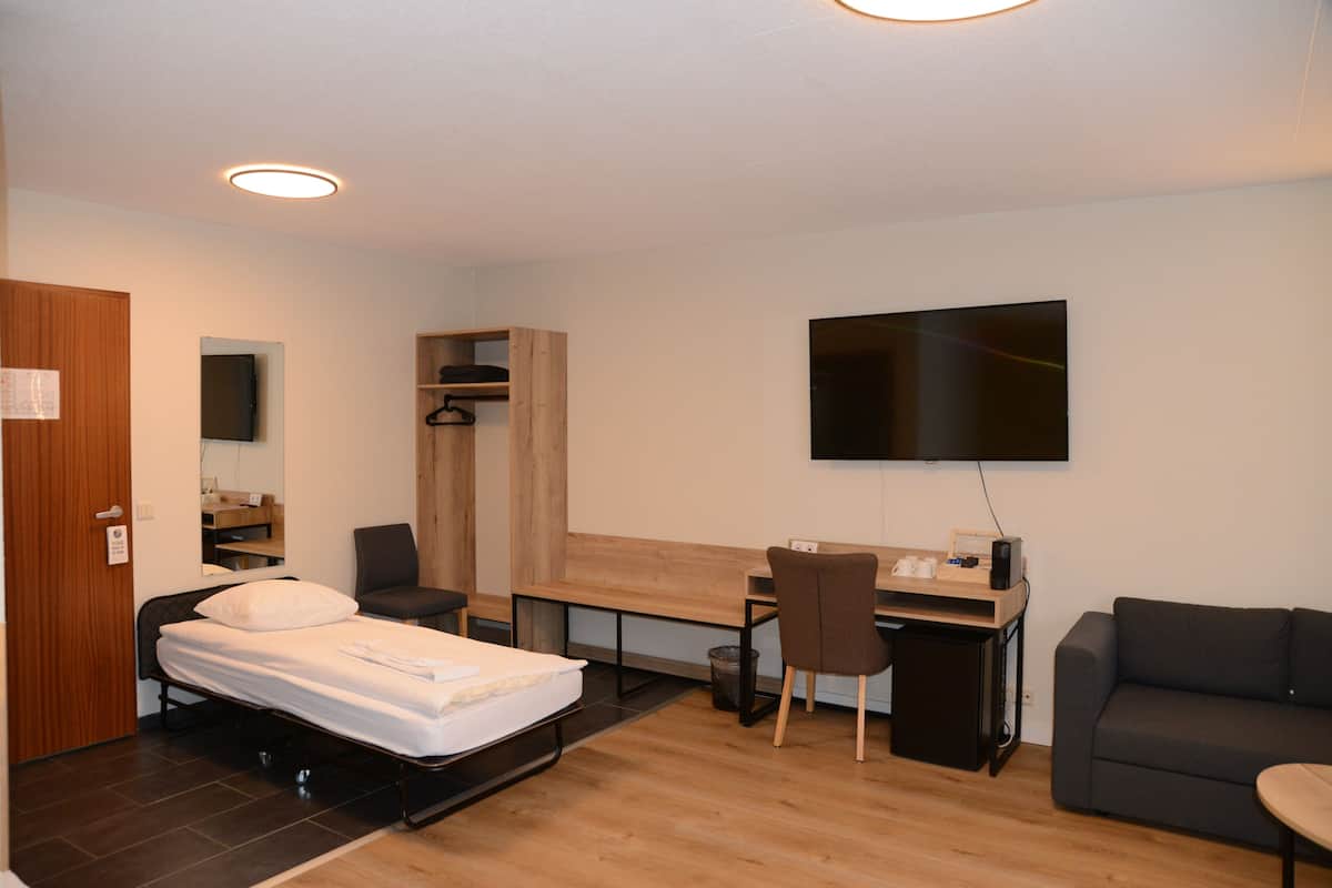 Una habitación compacta con cama, escritorio, silla, televisor y sofá.