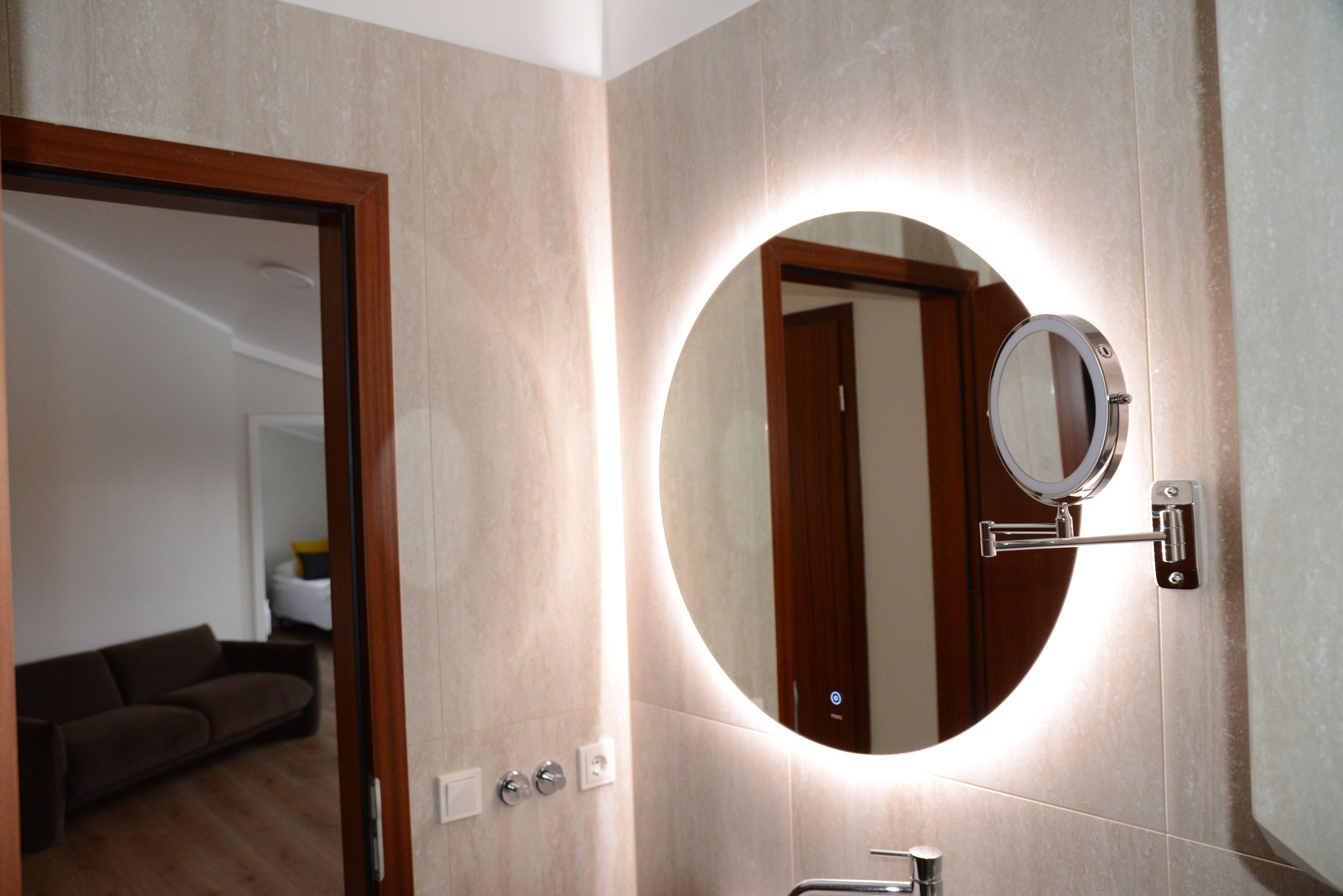 Un baño con un espejo redondo, un perchero y una puerta que da a una zona de estar.