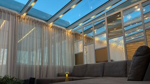 Ein modernes Wohnzimmer mit einer großen Eckcouch, transparenten Vorhängen und einem Oberlicht.
