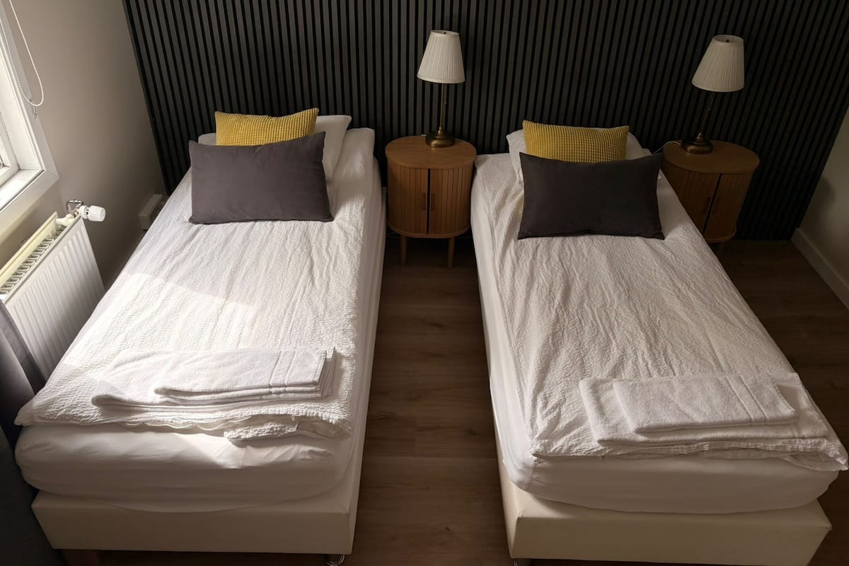 Una habitación con dos camas individuales, cada una con una almohada y una lámpara sobre una mesita de noche.