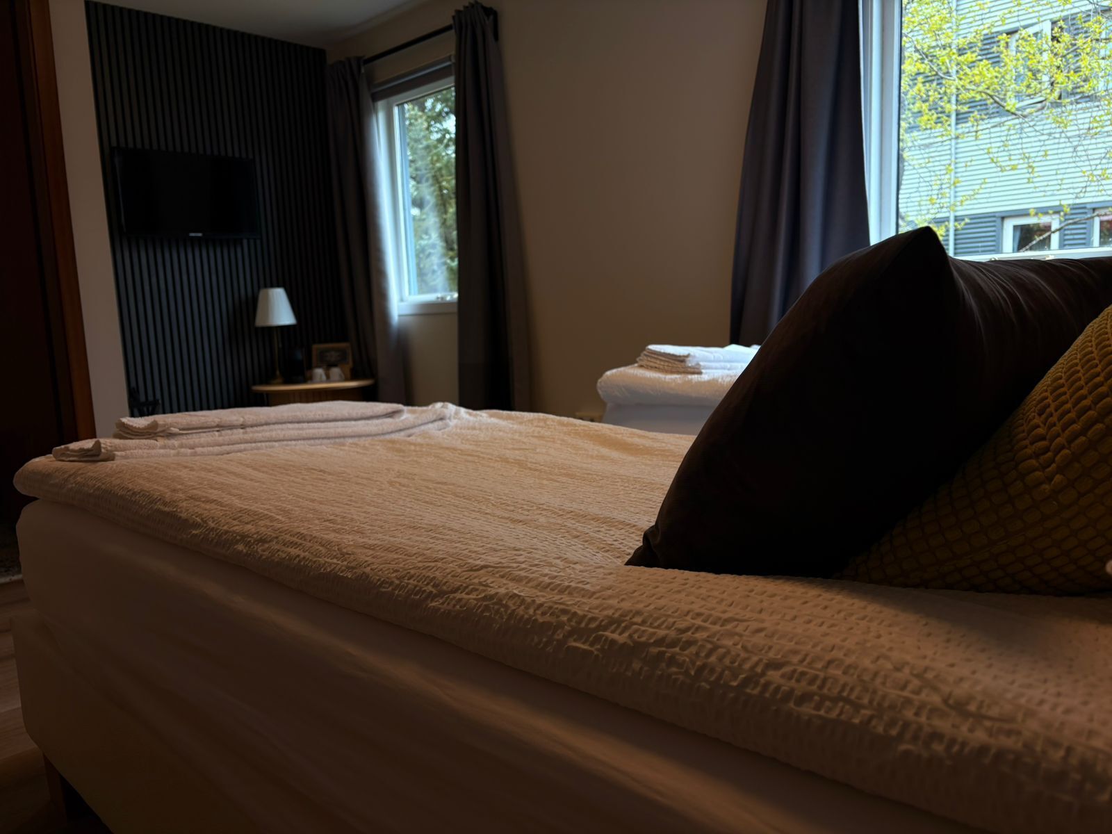 A hotel room with a bed, a TV mounted on the wall, a window with curtains, and a view of the outside.
