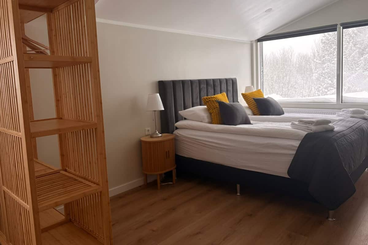 Un dormitorio con una cama, una mesita de noche, una lámpara, una ventana y un estante de madera.