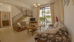 A living room with a sofa, coffee table, and a TV. There is a staircase leading to another room. - Aura Holiday Villas (Kissonerga)