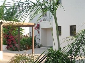 A modern building with a white exterior, a covered outdoor area with plants, and a clear sky.