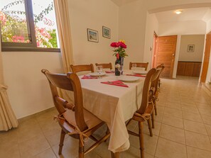 A dining room with a round table set for four, wooden chairs, a vase with flowers, and a window with curtains.