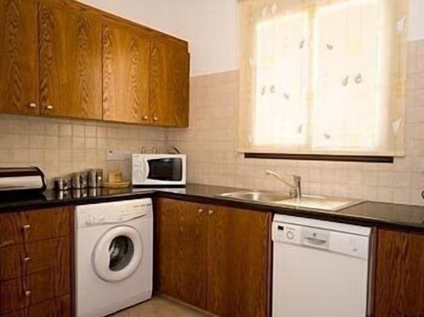 A kitchen with wooden cabinets, a microwave, a washing machine, and a dishwasher.