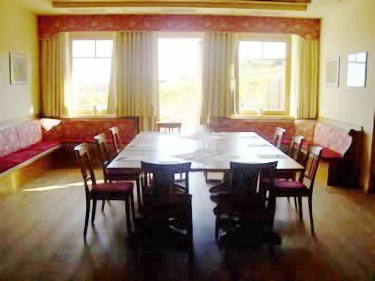 A dining room with a long table and chairs, a sofa, and large windows with curtains.