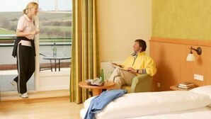 Quarto de hotel com cama, mesa de cabeceira, janela com cortinas e vista para o exterior.