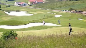 Um campo de golfe com bunkers, um clube e uma igreja ao fundo.