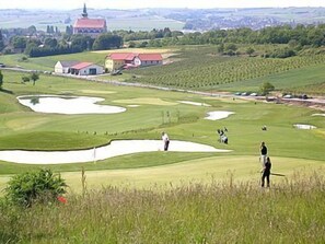 A golf course with bunkers, a clubhouse, and a church in the background. - Veltlin (Poysdorf)