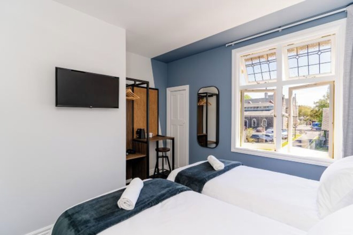 A hotel room with two beds, a TV, a wardrobe, a mirror, and a window with a view of the street.