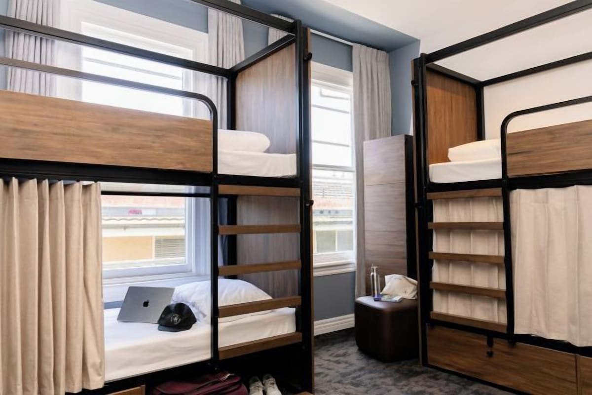 A hotel room with bunk beds, a laptop on one bed, a telephone, and a small table.