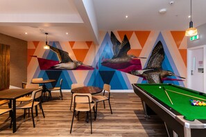 A billiards table with pool cues and balls, a wooden pool table, and a wall with a geometric pattern and bird sculptures. - Haka House Christchurch (Christchurch)