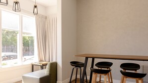Una cocina moderna con una mesa de madera y taburetes negros, un sofá gris y lámparas colgantes.