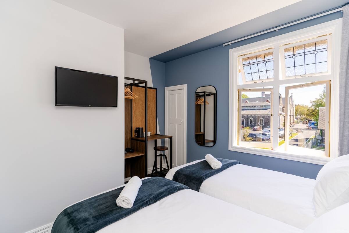 Habitación de hotel con dos camas, televisión, armario y ventana con vistas a la calle.