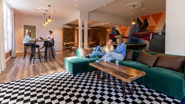 Un área de descanso moderna con piso a cuadros, sofás verdes y una mesa de centro de madera.