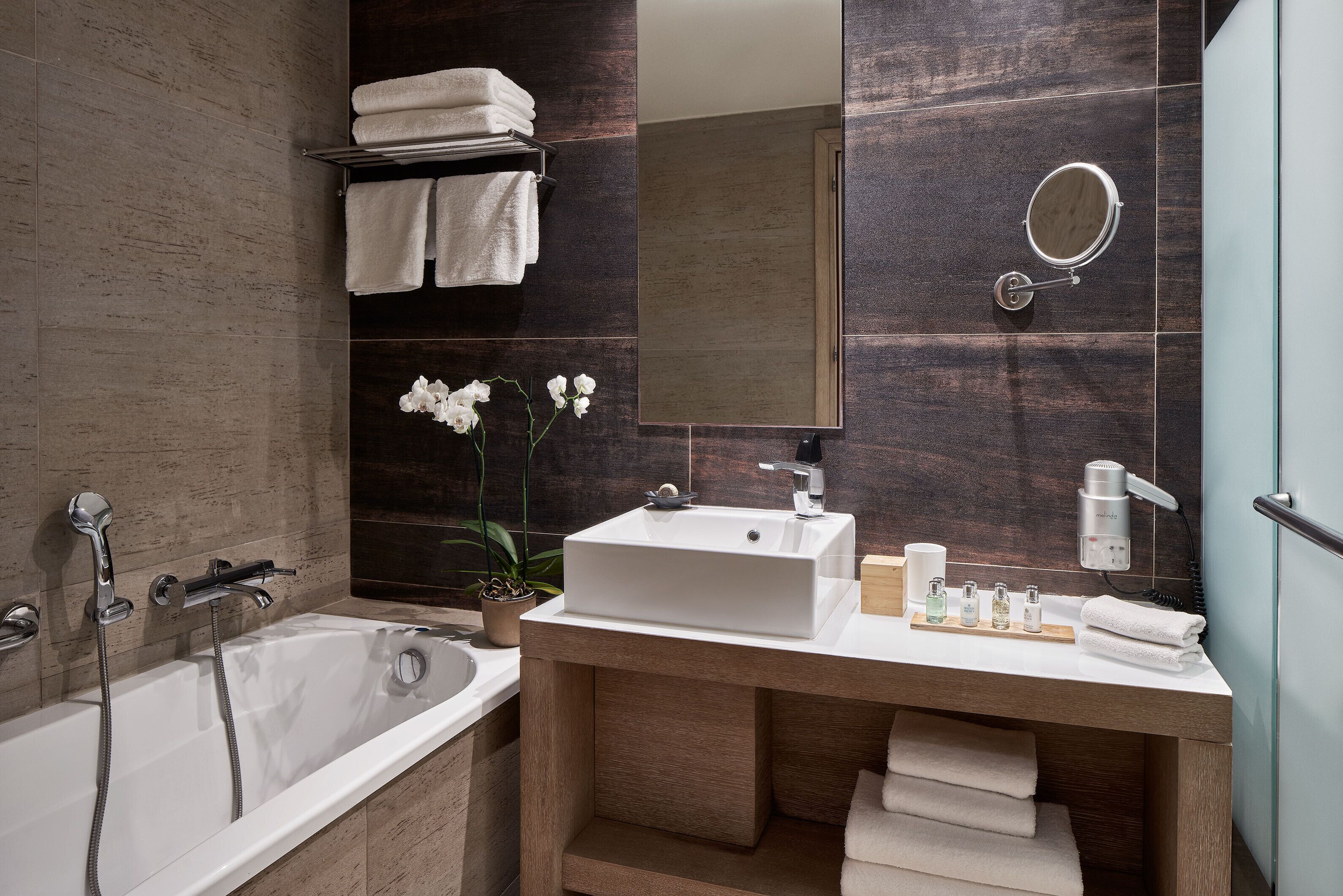 A modern bathroom with a bathtub, a sink, a mirror, and a towel rack.