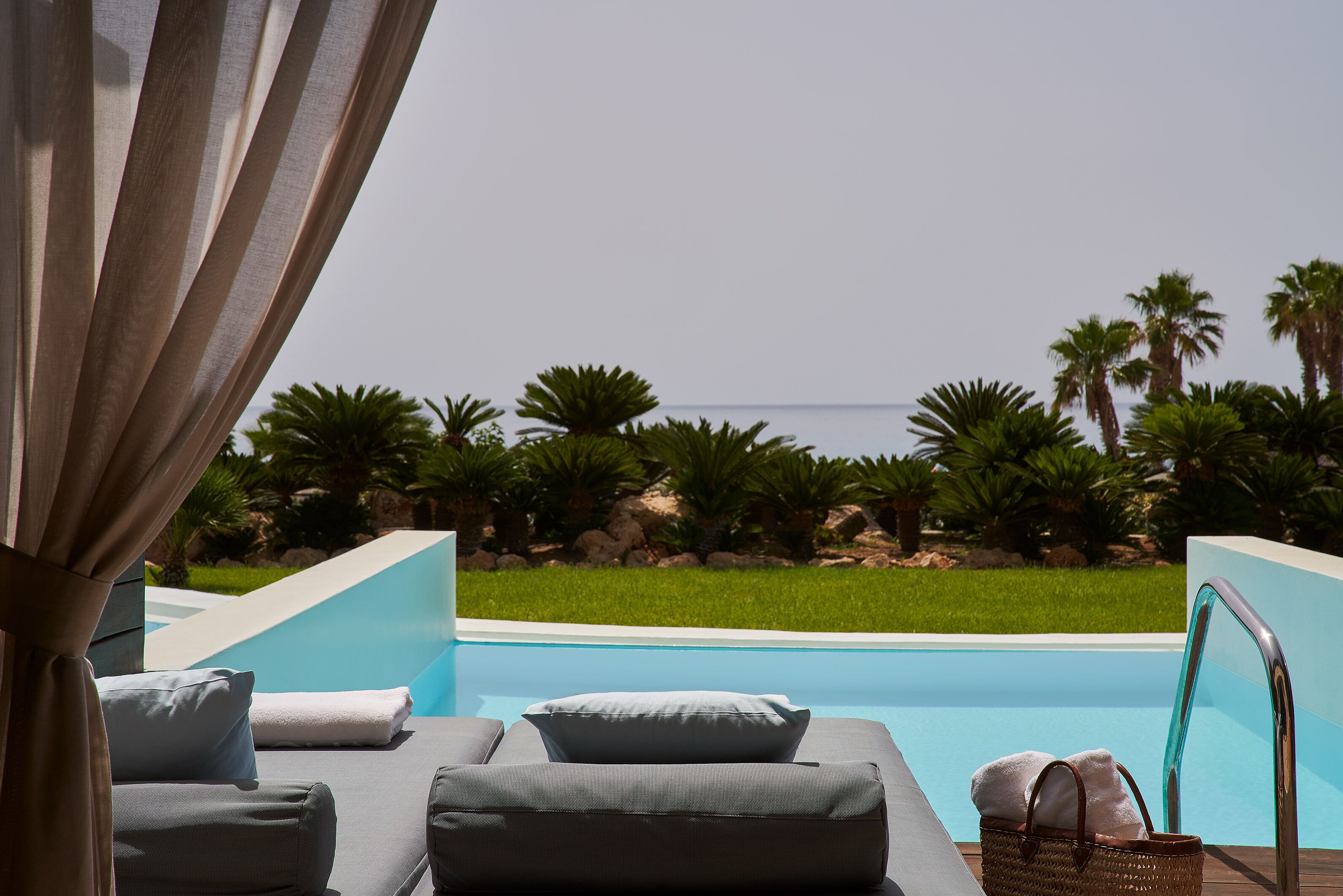 Un área de descanso junto a la piscina con vista al mar, una piscina y palmeras.