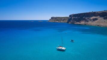 A coastal area with clear blue waters, a rocky cliff, and a sailboat.