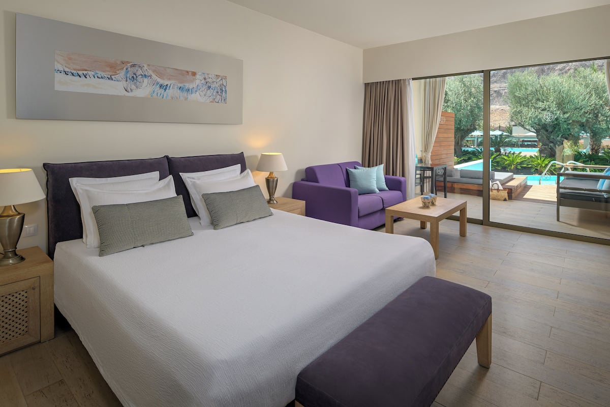 Une chambre d’hôtel avec un grand lit, un canapé, une petite table et une vue sur l’espace extérieur de la piscine.